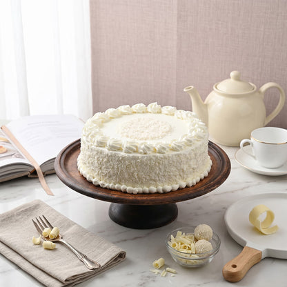 White Forest Cake decorated with white chocolate shards, whipped cream and red cherries.