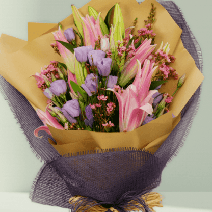 Pink lilies, lavender Eustoma and statice with fillers in purple and mustard non-woven wrapping