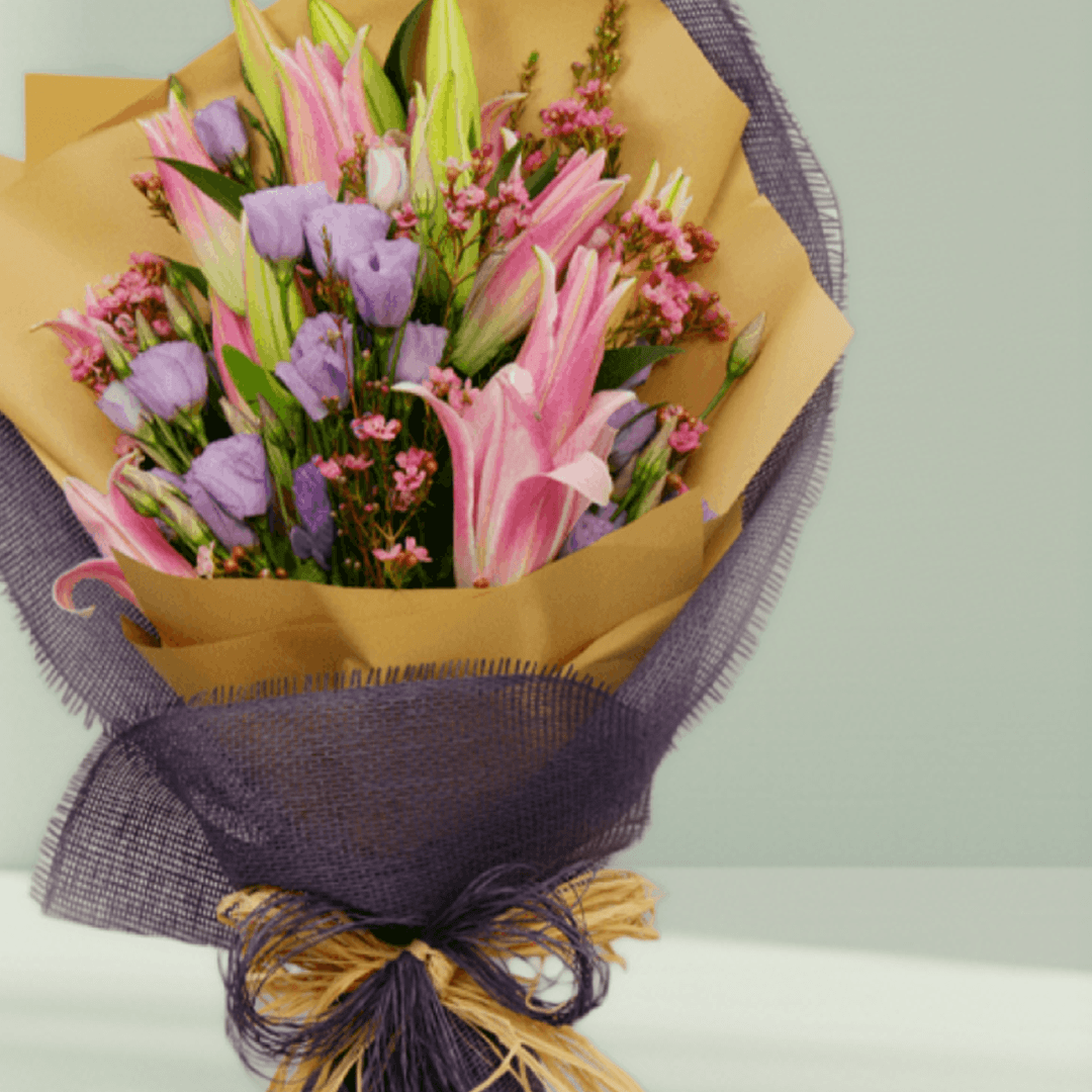 Pink lilies, lavender Eustoma and statice with fillers in purple and mustard non-woven wrapping