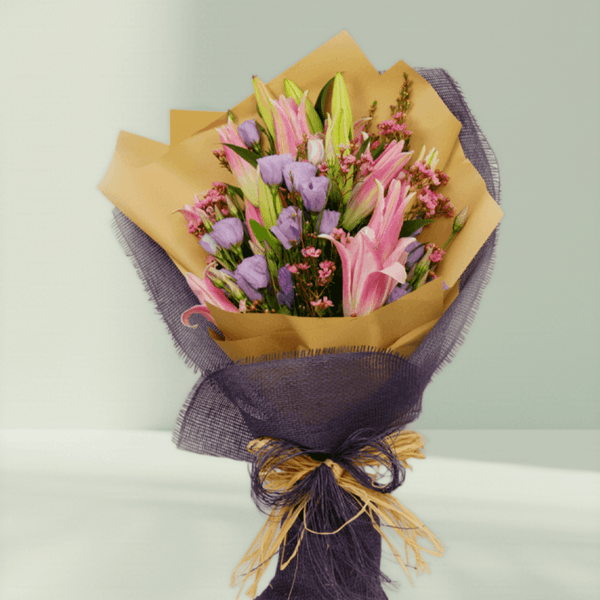 Pink lilies, lavender Eustoma and statice with fillers in purple and mustard non-woven wrapping