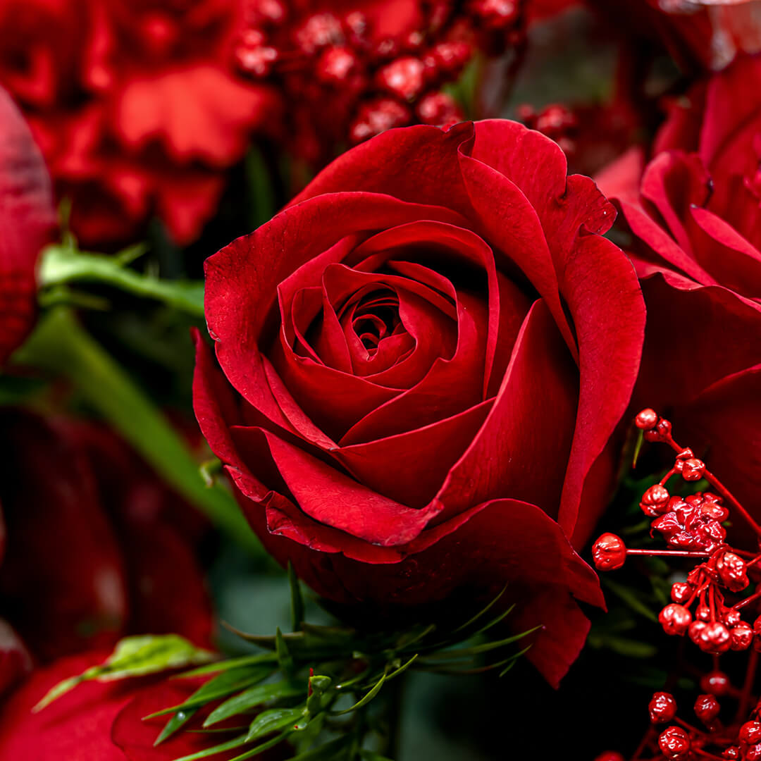 A fresh festive flower wreath with roses, carnations, eucalyptus, gypsophila, fresh greenery, and an LED taper candle.