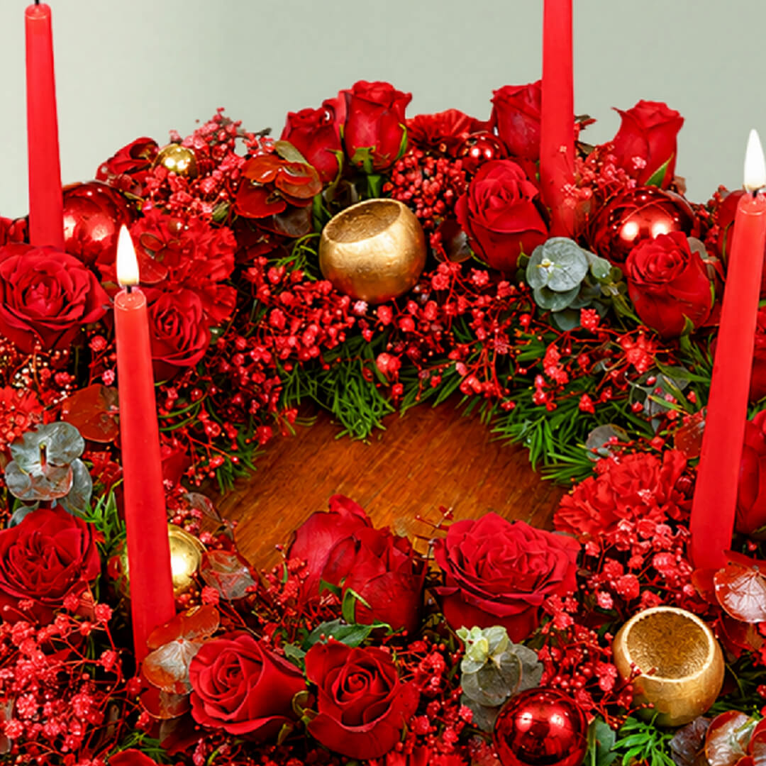 A fresh festive flower wreath with roses, carnations, eucalyptus, gypsophila, fresh greenery, and an LED taper candle.