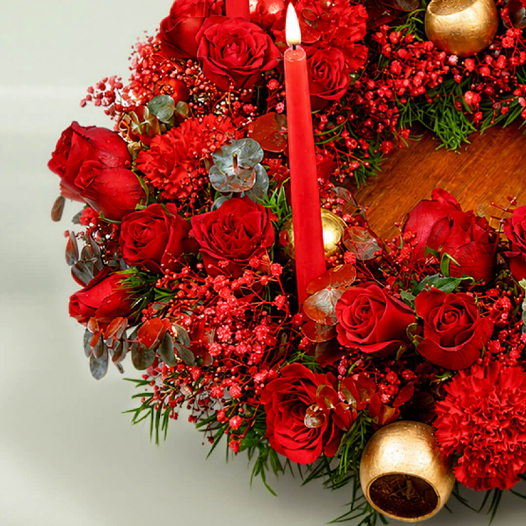 A fresh festive flower wreath with roses, carnations, eucalyptus, gypsophila, fresh greenery, and an LED taper candle.