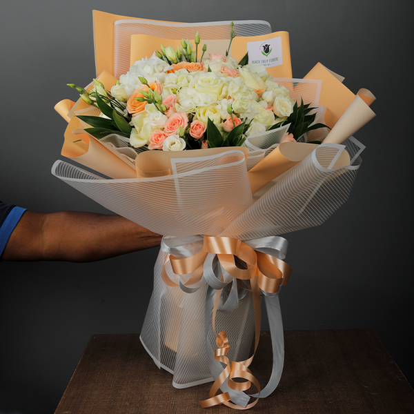 Bouquet featuring roses, spray roses, Eustoma and greenery in peach and grey Korean-style wrapping, finished with coordinating ribbons.
