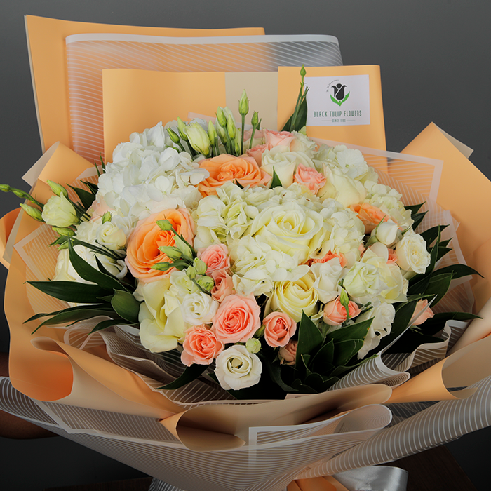 Bouquet featuring roses, spray roses, Eustoma and greenery in peach and grey Korean-style wrapping, finished with coordinating ribbons.