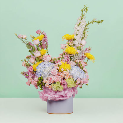A white round box featuring 30 stems of hydrangeas, delphiniums, disbuds, roses, eustoma, spray carnations, and hypericum artistically arranged.