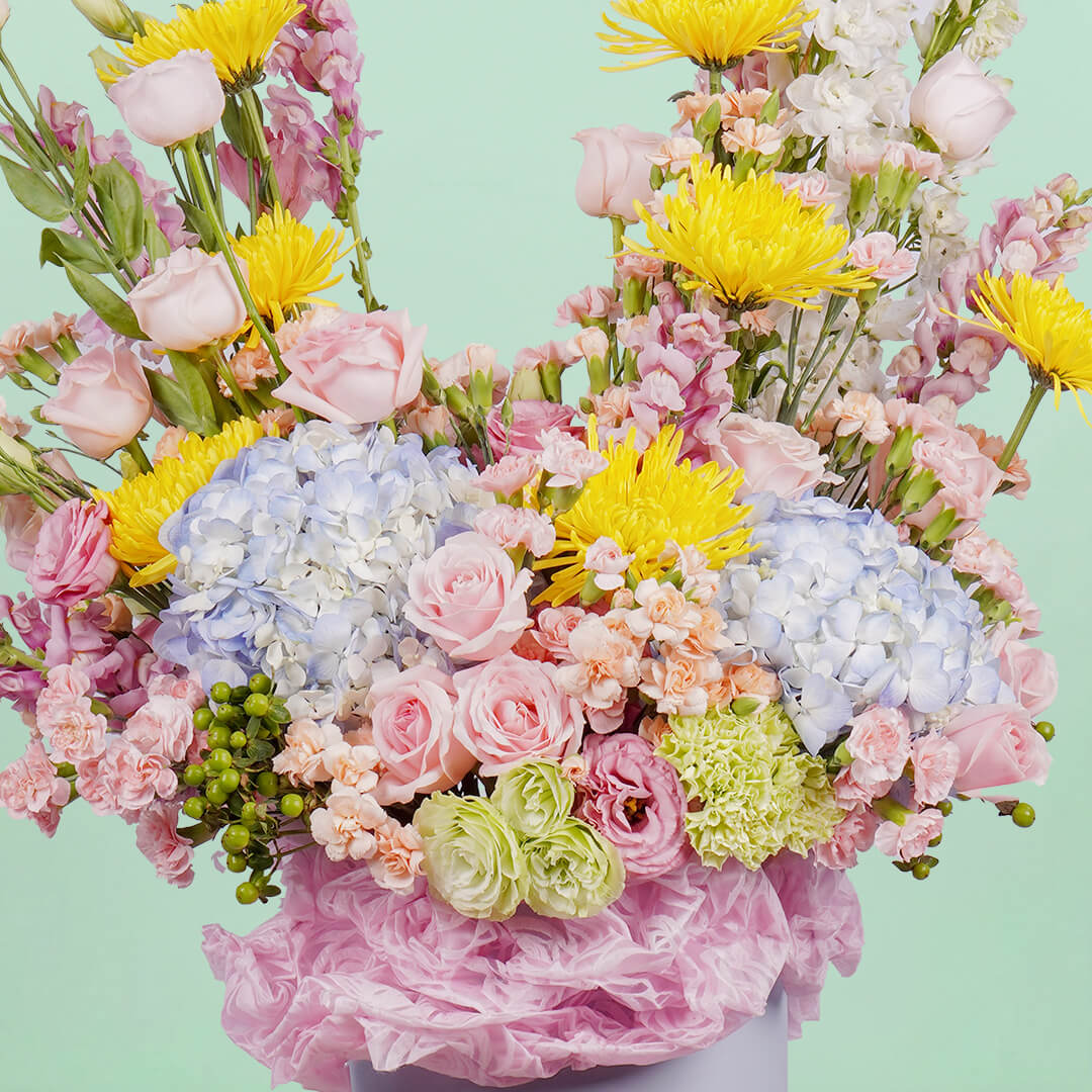 A white round box featuring 30 stems of hydrangeas, delphiniums, disbuds, roses, eustoma, spray carnations, and hypericum artistically arranged.