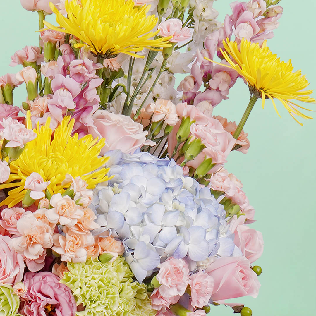 A white round box featuring 30 stems of hydrangeas, delphiniums, disbuds, roses, eustoma, spray carnations, and hypericum artistically arranged.