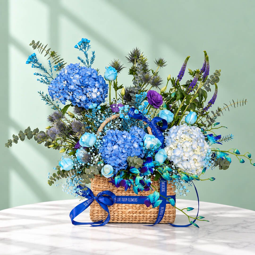 Rectangle basket filled with blue hydrangea, roses, orchid, veronica, and eustoma.