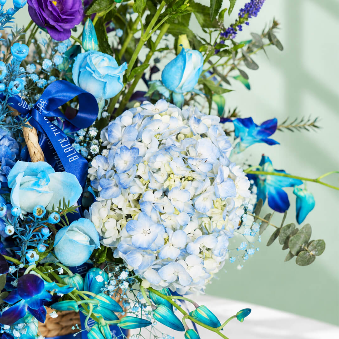 Rectangle basket filled with blue hydrangea, roses, orchid, veronica, and eustoma.