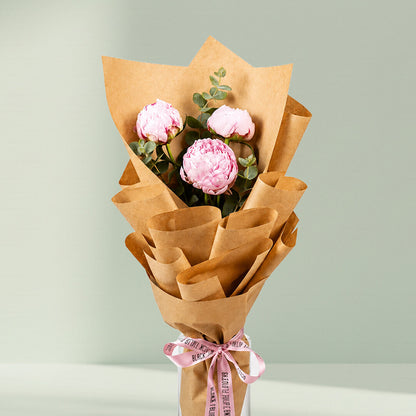 Blushing pink peony trio bouquet with fresh green fillers wrapped in elegant brown paper