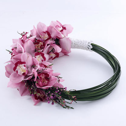 A loop-style bridal bouquet featuring pink Cymbidium orchids and delicate accent flowers in finished with a white lace handle.