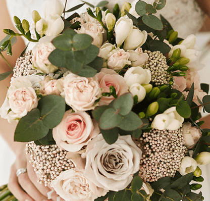 A hand-tied bouquet featuring blush pink roses, seasonal flowers and eucalyptus greenery.