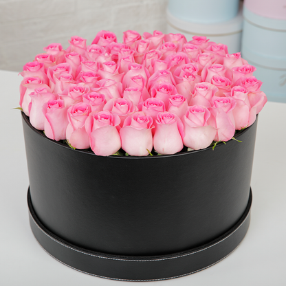 Round flower box featuring fresh pink roses in a sleek black base.