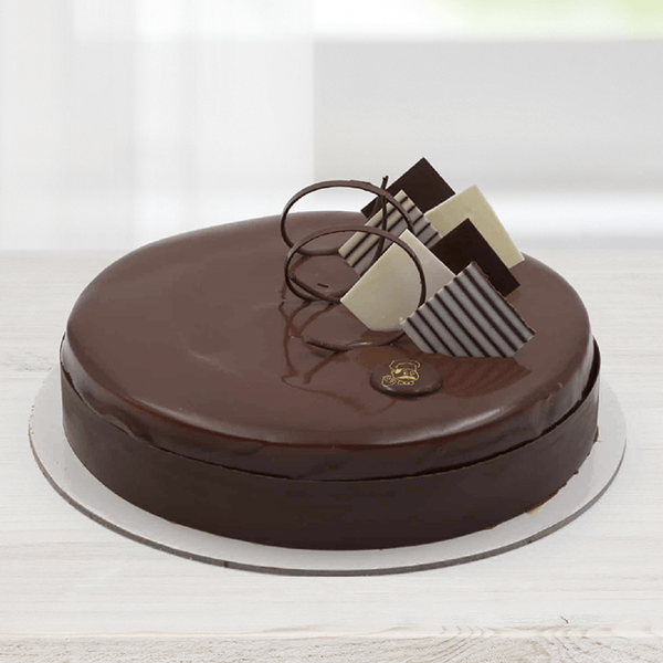 Chocolate mousse cake featuring a glossy chocolate glaze, chocolate curls and decorative dark and white chocolate pieces.