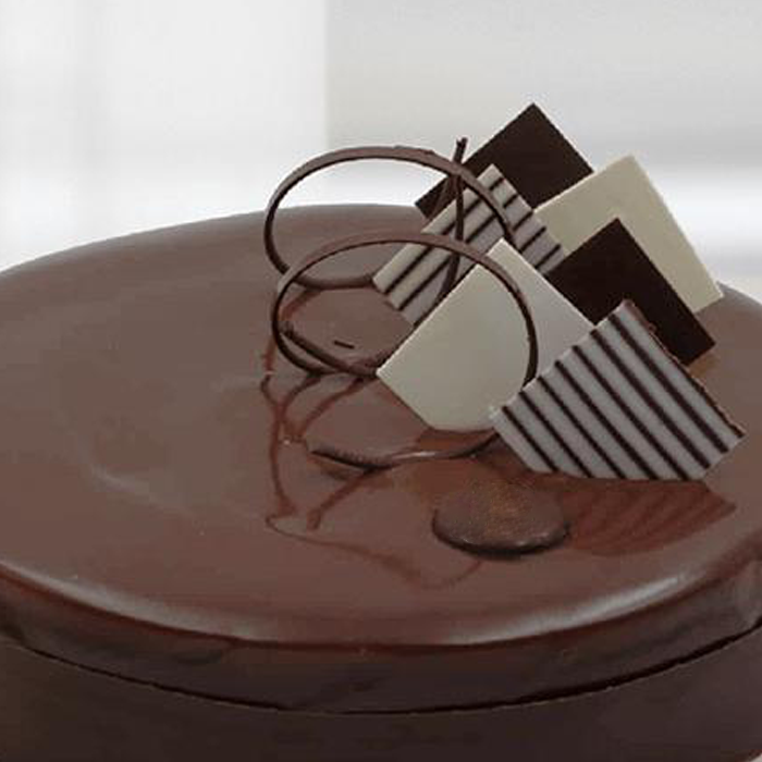 Chocolate mousse cake featuring a glossy chocolate glaze, chocolate curls and decorative dark and white chocolate pieces.