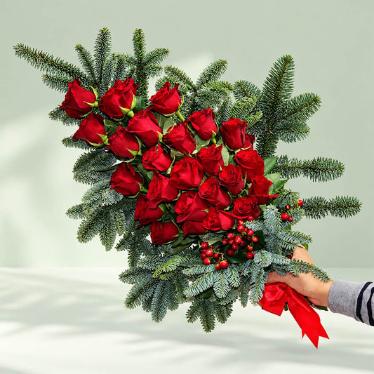 Christmas hand bouquet featuring vibrant red roses and lush pine branches for festive holiday flower gifting