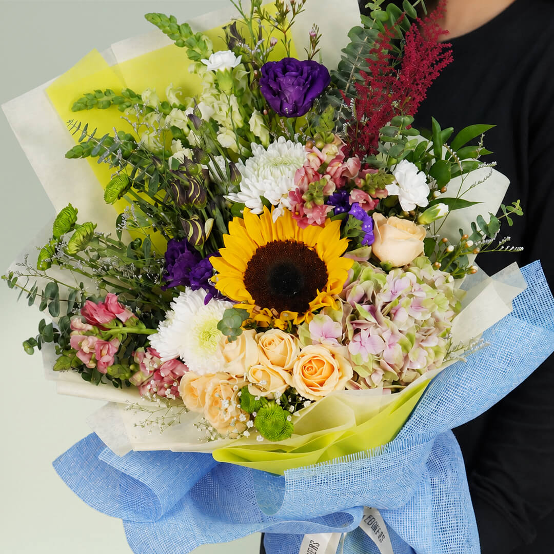 Classic mixed flower bouquet with sunflower, roses, hydrangea, snapdragon and fresh greenery in blue wrapping