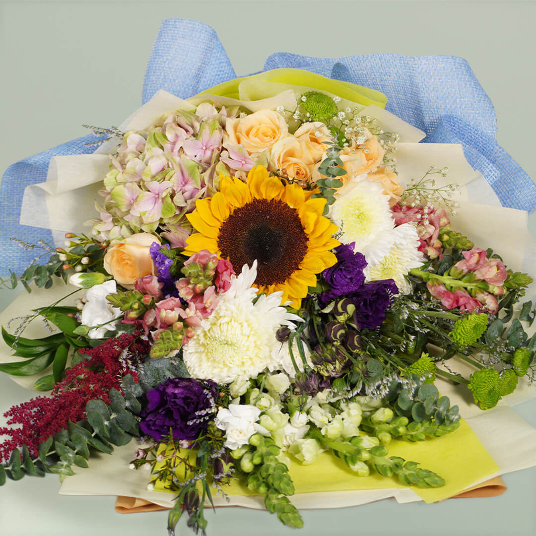 Classic mixed flower bouquet with sunflower, roses, hydrangea, snapdragon and fresh greenery in blue wrapping