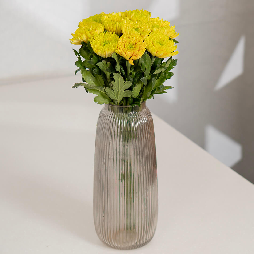 Fresh Disbud flowers neatly arranged in ribbed clear glass vase.
