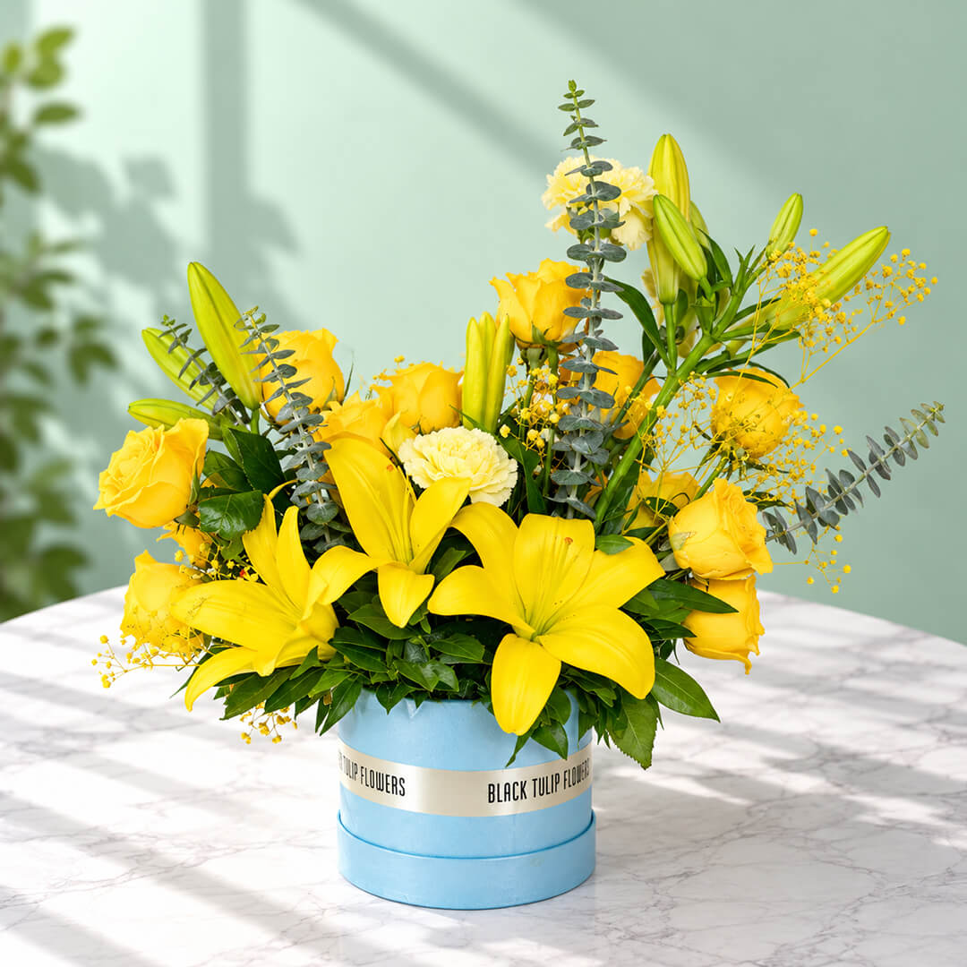 Yellow rose, carnation and lily flower arrangement with gypsophila and eucalyptus, presented in a round blue flower box.