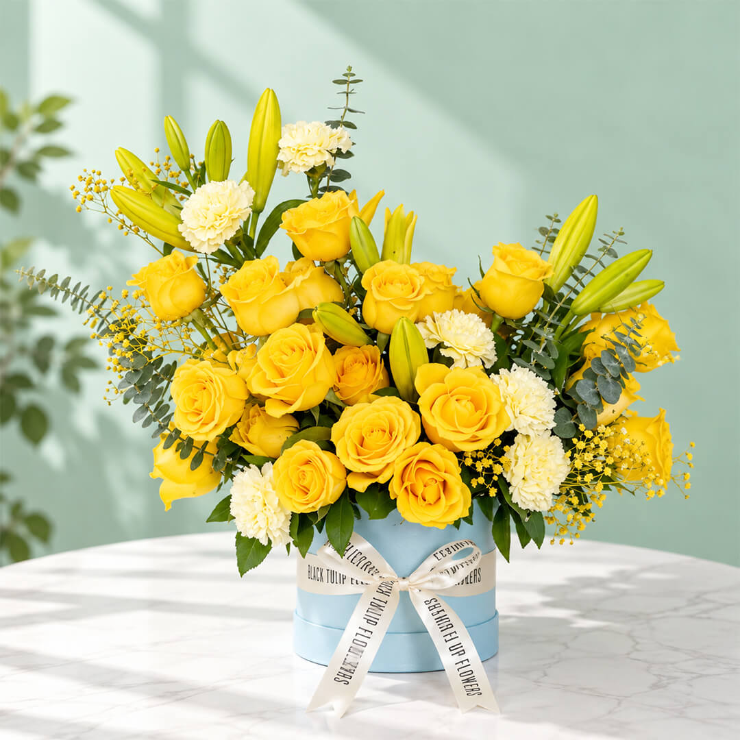 Yellow rose, carnation and lily flower arrangement with gypsophila and eucalyptus, presented in a round blue flower box.