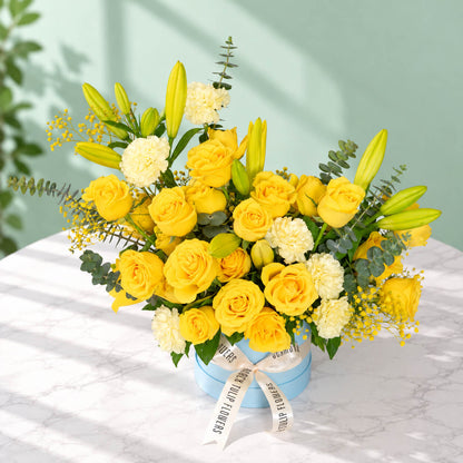 Yellow rose, carnation and lily flower arrangement with gypsophila and eucalyptus, presented in a round blue flower box.