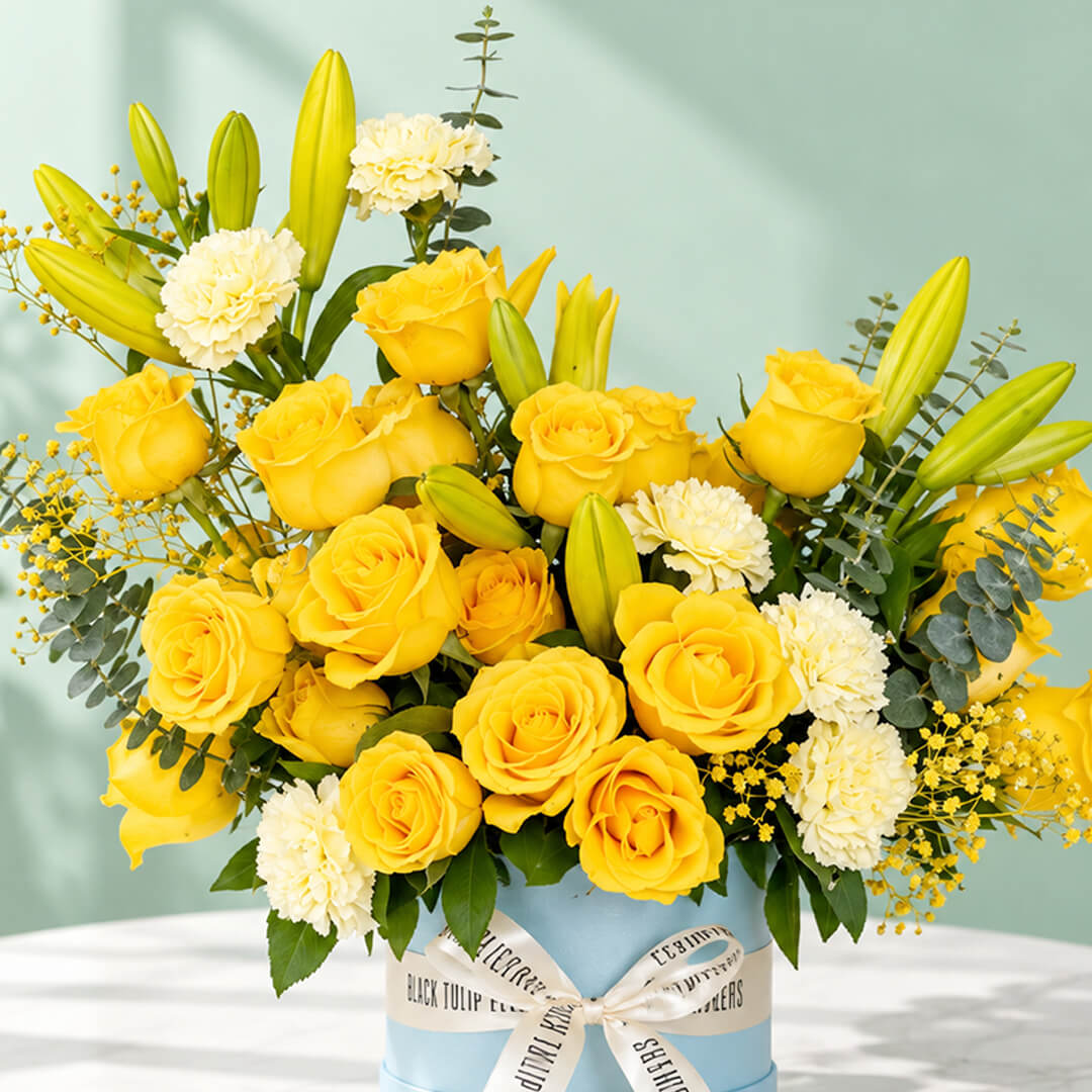 Yellow rose, carnation and lily flower arrangement with gypsophila and eucalyptus, presented in a round blue flower box.