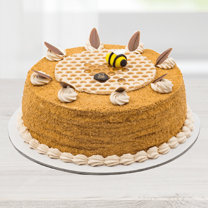 Honey cake featuring a fine crumb coating, cream swirls, chocolate decorations and a bee topper.