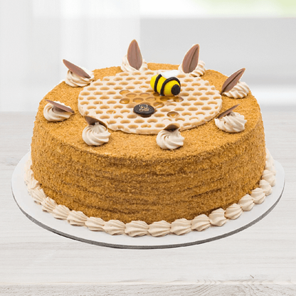 Honey cake featuring a fine crumb coating, cream swirls, chocolate decorations and a bee topper.