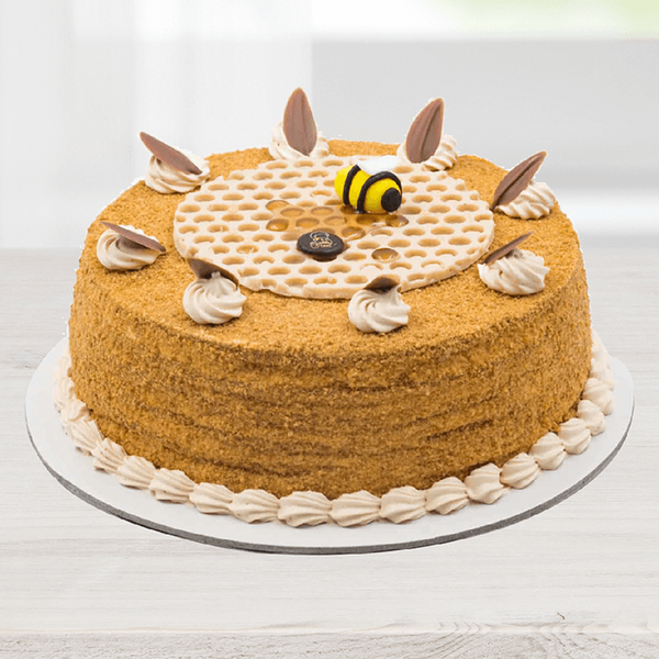 Honey cake featuring a fine crumb coating, cream swirls, chocolate decorations and a bee topper.
