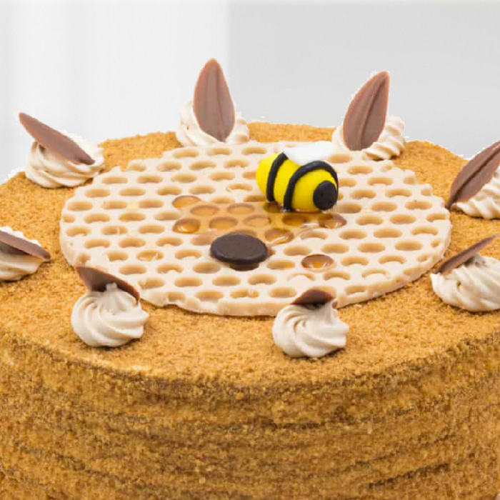 Honey cake featuring a fine crumb coating, cream swirls, chocolate decorations and a bee topper.