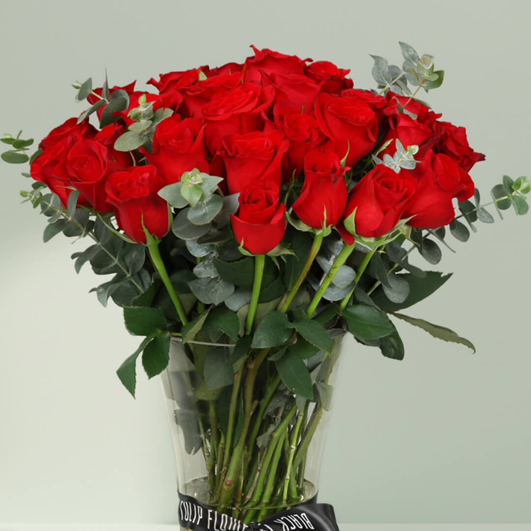 25 fresh red roses with greenery arranged in a clear hourglass glass vase