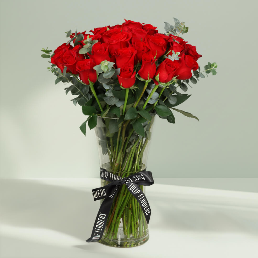 25 fresh red roses with greenery arranged in a clear hourglass glass vase