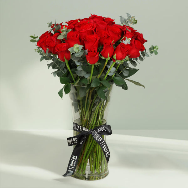 25 fresh red roses with greenery arranged in a clear hourglass glass vase