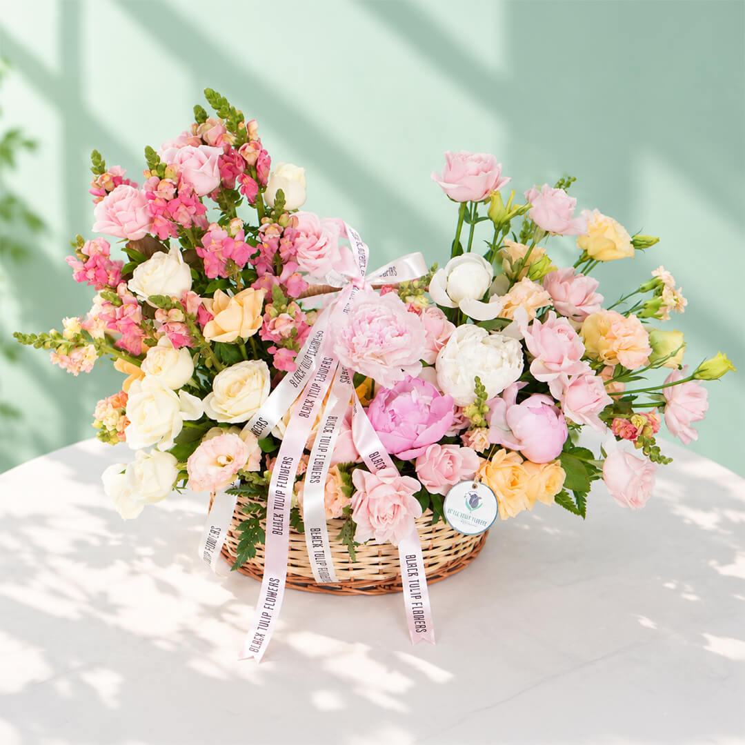 Mixed blooms including roses, peonies, carnations and snapdragons arranged in a basket