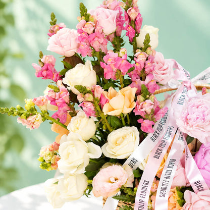 Mixed blooms including roses, peonies, carnations and snapdragons arranged in a basket