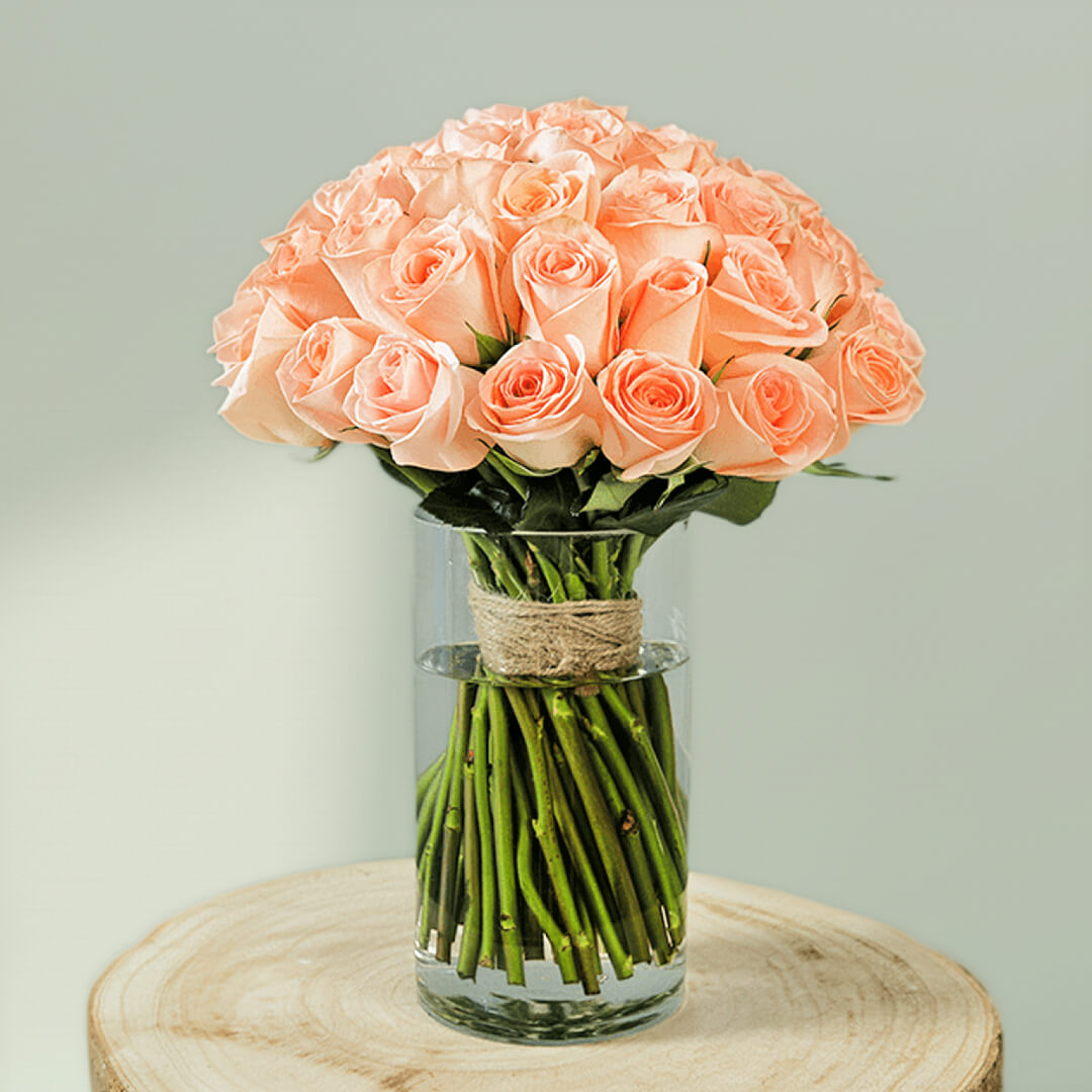 30 handpicked peach roses with rich green foliage in a modern transparent glass vase.