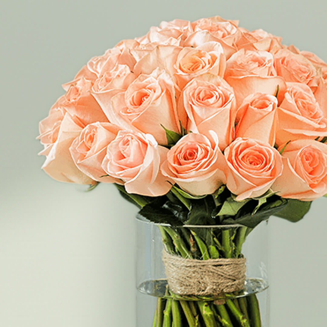 30 handpicked peach roses with rich green foliage in a modern transparent glass vase.