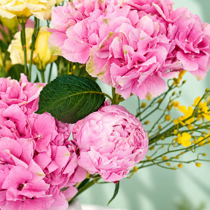 Pink and yellow flower arrangement with peony, hydrangea and orchids in a ceramic vase