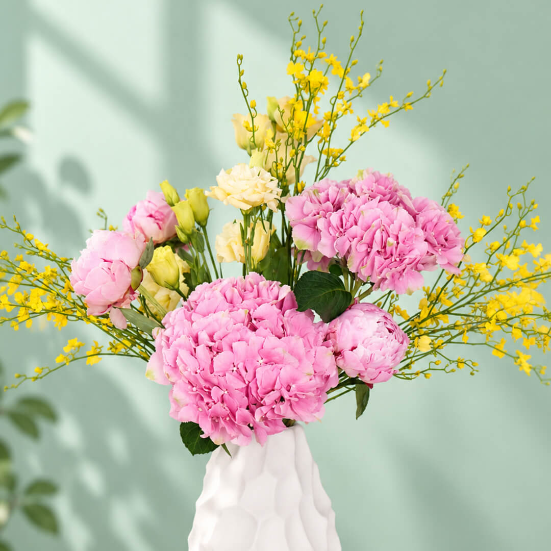 Pink and yellow flower arrangement with peony, hydrangea and orchids in a ceramic vase