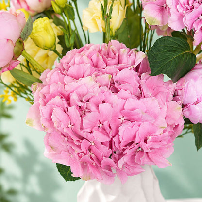 Pink and yellow flower arrangement with peony, hydrangea and orchids in a ceramic vase