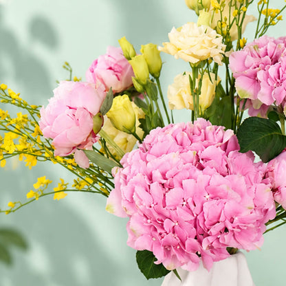 Pink and yellow flower arrangement with peony, hydrangea and orchids in a ceramic vase