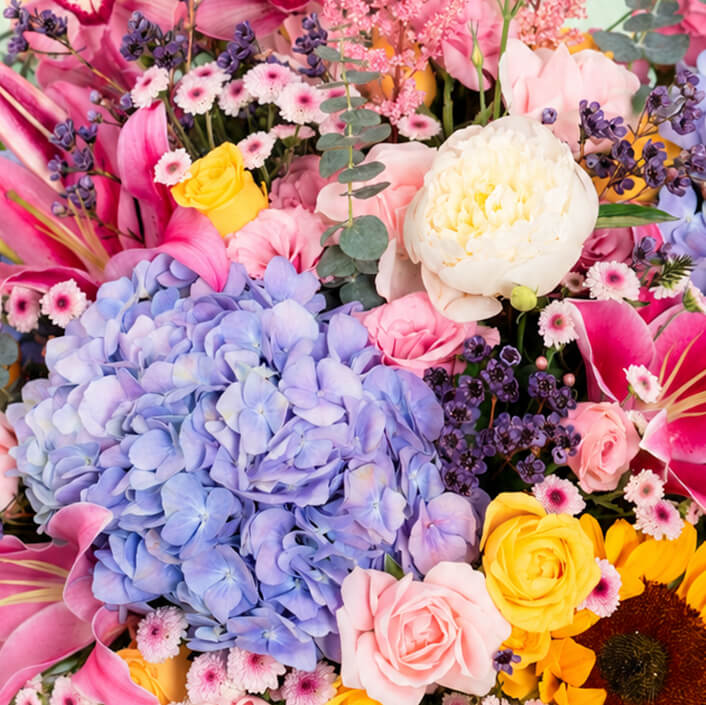 Pink round flower box featuring 50–60 stems of assorted hydrangeas, peonies, sunflowers, tulips, roses, lilies, cymbidium orchids and eucalyptus greenery.