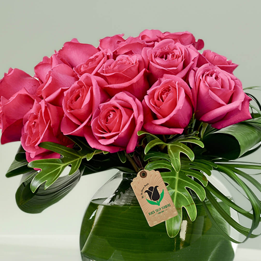 Pink roses and decorative tropical greenery in a transparent fish bowl glass vase.