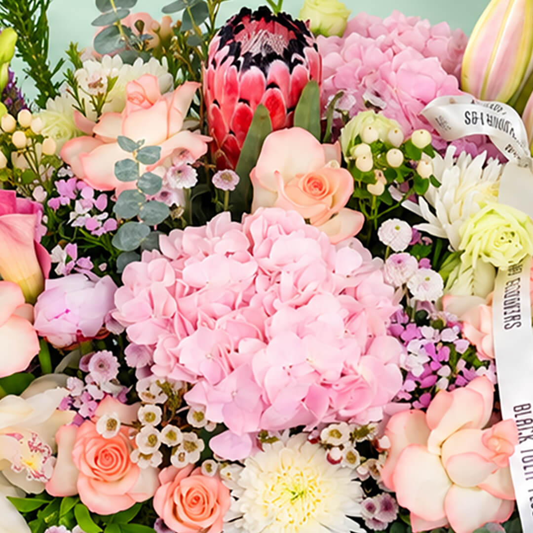 Assorted flowers including roses, hydrangea, calla lily, cymbidium, and Queen Protea arranged in a rectangular basket