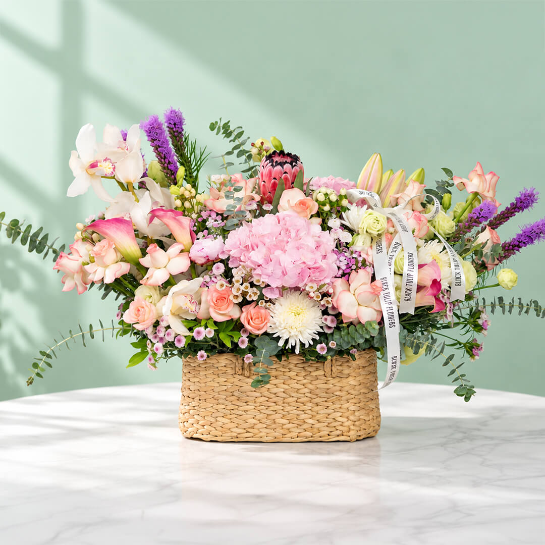 Assorted flowers including roses, hydrangea, calla lily, cymbidium, and Queen Protea arranged in a rectangular basket