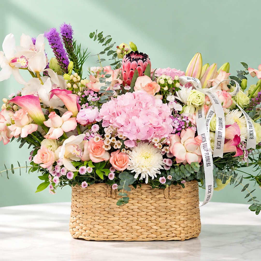 Assorted flowers including roses, hydrangea, calla lily, cymbidium, and Queen Protea arranged in a rectangular basket