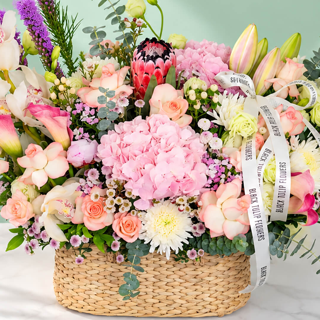 Assorted flowers including roses, hydrangea, calla lily, cymbidium, and Queen Protea arranged in a rectangular basket
