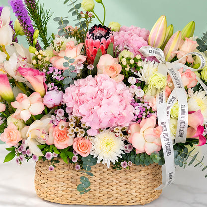 Assorted flowers including roses, hydrangea, calla lily, cymbidium, and Queen Protea arranged in a rectangular basket